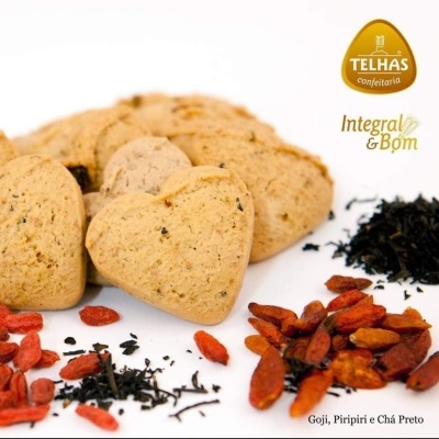Bolachas em forma de coração com sementes, bagas de goji, piri-piris vermelhos secas, chá preto seco, fundo branco, logotipo TELHAS confeitaria Integral & Bom
