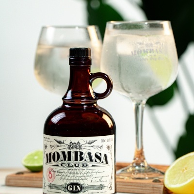 Garrafa de gin Mombasa Club com taças e limão num fundo claro.