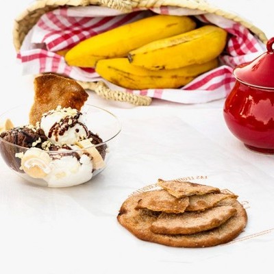 Taça com gelado, bolachas, bananas e pote vermelho sobre mesa branca