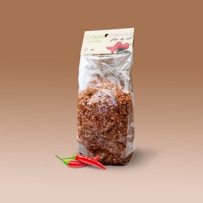 Pacote de cristais de flor de sal com pimentas vermelhas sobre fundo castanho