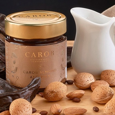 Frasco de creme Carob com amêndoas e leite de caramelo rodeado de ingredientes naturais