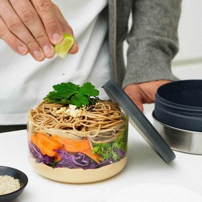 Frasco transparente com salada em camadas e mão a espremer lima em cozinha clara