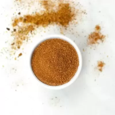 Pó castanho avermelhado em recipiente branco com pó espalhado à volta