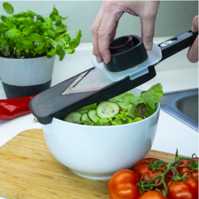 Mandoline preto com lâmina metálica a fatiar pepino em salada numa tigela branca