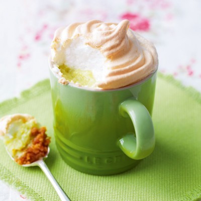 Caneca verde com recheio amarelo e suspiro tostado, colher com recheio, tecido verde e fundo floral