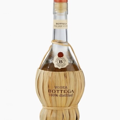 Garrafa de vodka Bottega com revestimento em palha clara, tampa laranja e rótulos com texto.