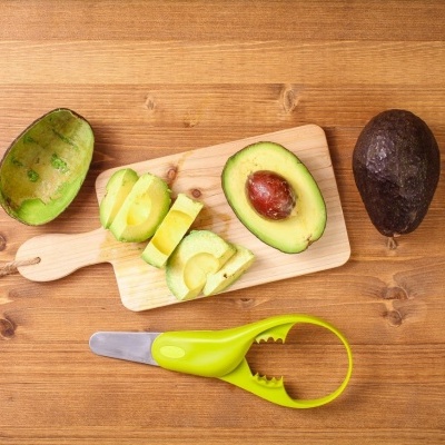 Dois abacates e cortador de abacate verde sobre mesa de madeira