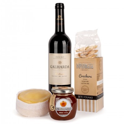 Conjunto com garrafa de vinho tinto, queijo redondo, pote de compota e embalagem de crackers