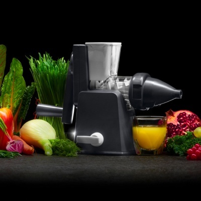 Máquina de sucos manual preta com copo de vidro e frutas ao redor