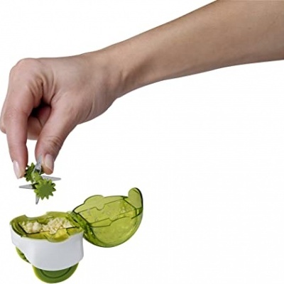 Dispositivo de cozinha verde e branco com tampo aberto e mão a colocar peça verde