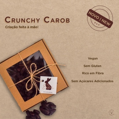 Embalagem de Crunchy Carob amarrada com fio de juta e etiquetas, sobre fundo castanho com texto em castanho.