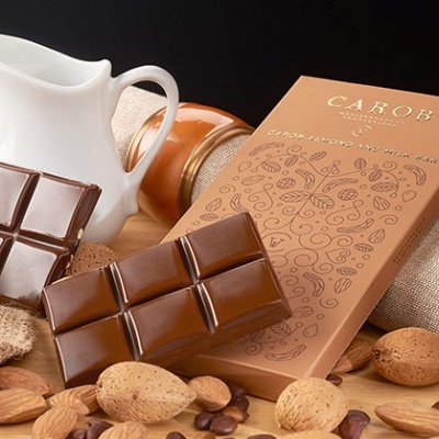 Barra de chocolate com caixa e amêndoas sobre uma superfície de madeira