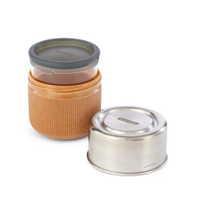 Frasco de vidro com tampa cinza e capa castanha ao lado de recipiente metálico prateado