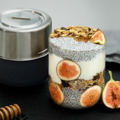 Pote de vidro com iogurte, sementes de chia, granola e fatias de figo num fundo preto.