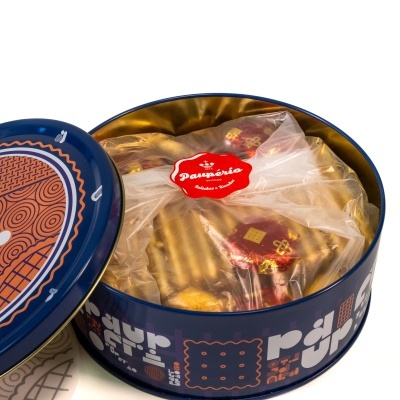 Lata azul redonda com doces embalados em papel vermelho dentro de embalagem transparente.