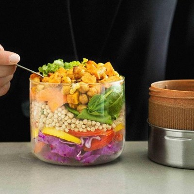 Recipiente transparente com camadas de alimentos variados e tigela térmica em inox e cortiça ao lado