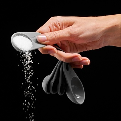 Conjunto de colheres medidoras cinza seguradas por mão humana despejando açúcar.