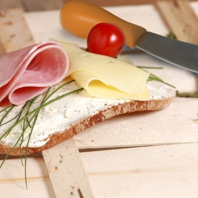 Pão com queijo creme, fiambre, queijo fatiado, cebolinho e tomate cereja numa tábua de madeira