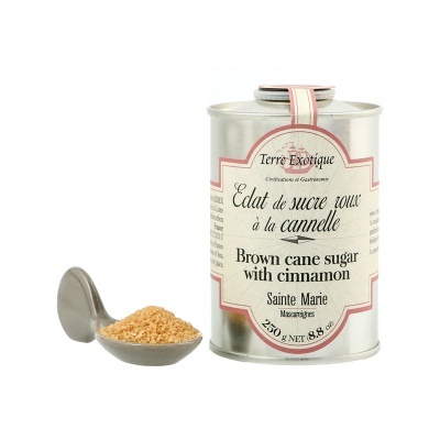 Lata metálica de açúcar mascavado com canela ao lado de uma colher com açúcar mascavado