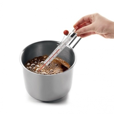 Caneca metálica prateada com termómetro e líquido escuro a ferver