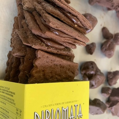 Pacote amarelo de biscoitos DIPLOMATA BISCUIT com biscoitos de chocolate recheados e pedaços de chocolate ao lado.