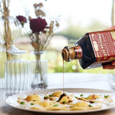 Frasco de vinagre balsâmico a ser derramado sobre prato de massa branca com molho