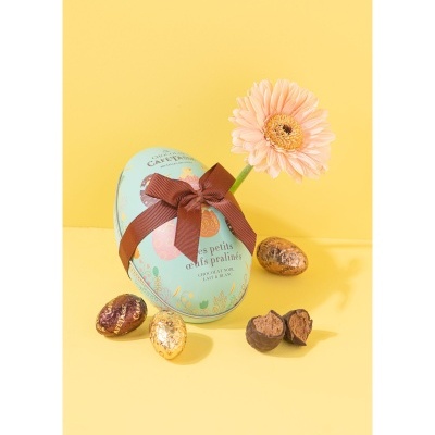 Caixa oval azul com laço castanho, ovos de chocolate e flor rosa sobre fundo amarelo