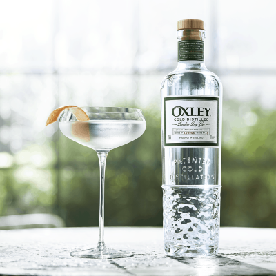 Garrafa de gin OXLEY e copo de cocktail com limão num ambiente exterior