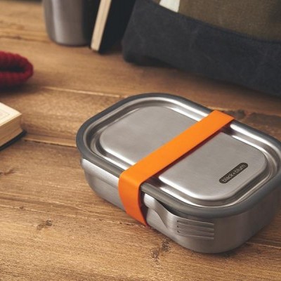 Caixa de almoço metálica prateada com elástico laranja sobre mesa de madeira