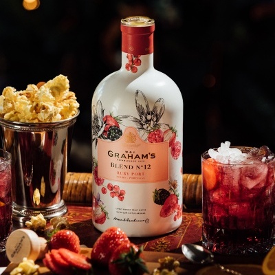 Garrafa branca Graham's Blend Nº 12 Ruby Port com bebida vermelha, pipoca e frutas sobre madeira