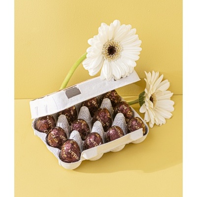 Caixa de ovos de chocolate prateados e roxos numa caixa de ovos branca com flores brancas ao lado
