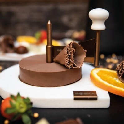 Bolo redondo de chocolate com decoração de folhas de chocolate e fatia de laranja