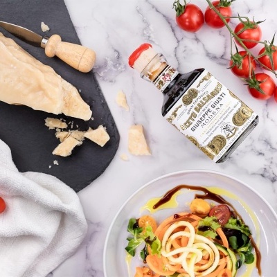 Pedaço de queijo Parmigiano Reggiano, frasco de azeite trufado, tomate cherry e salada num prato