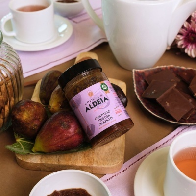 Frasco de compota de goiaba com chocolate Aldeia com figos, chávena e chocolate sobre mesa com toalha rosa.