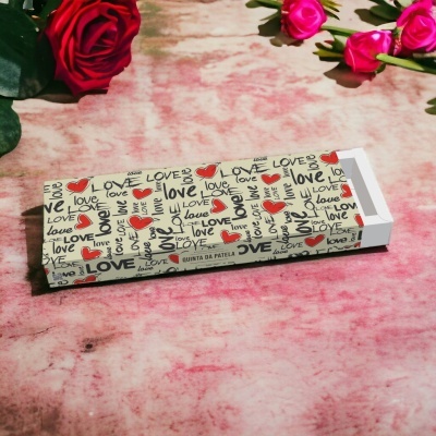 caixa branca com padrões de 'love' e corações, marca Quinta da Patela, sobre fundo cor-de-rosa com rosas