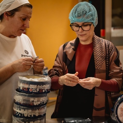 Duas mulheres a embalar tabletes de chocolate numa mesa num ambiente interior.