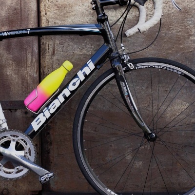 Bicicleta de corrida Bianchi preta encostada numa parede de metal