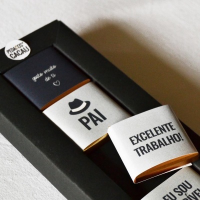 Barras de chocolate com embalagens brancas e pretas com mensagens em português dentro de uma caixa preta