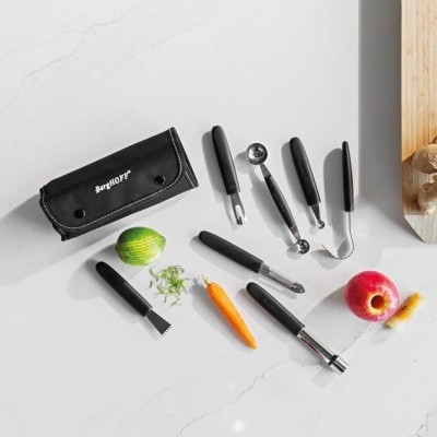 Utensílios de cozinha com cabo preto e frutas sobre bancada branca ao lado de tábua de madeira.