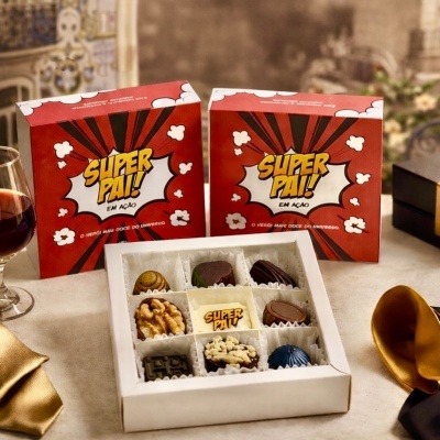 Caixa de bombons variados com embalagem vermelha SUPER PAI! e mesa decorada com vinho e guardanapo dourado.