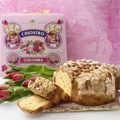 Bolo italiano Colomba com cobertura de amêndoas ao lado de caixa rosa Chiostro e tulipas vermelhas
