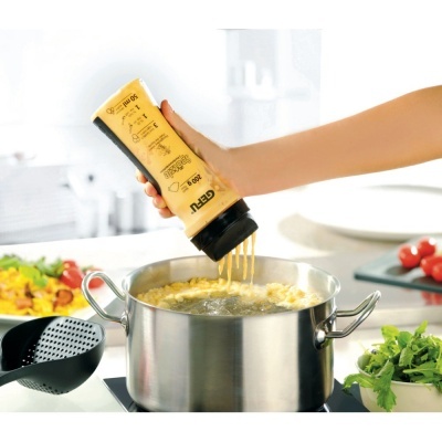 Frasco amarelo com líquido a ser despejado em panela de aço inox a ferver no fogão com salada ao lado