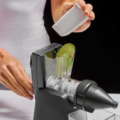 Processador de alimentos preto com frutas verdes e peça branca sendo segurada