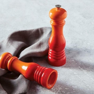 Dois moedores de especiarias em madeira laranja sobre pano cinzento e superfície cinzenta.