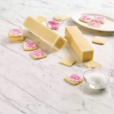 Barras de manteiga, bolachas decoradas com granulados rosa, tigelas com granulados e sal sobre mesa de mármore