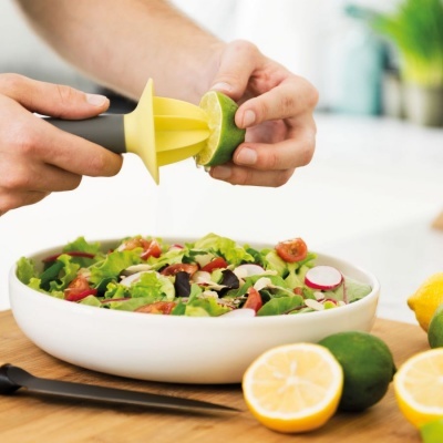 Espremedor de limão amarelo com cabo cinza a espremer limão sobre salada em prato branco
