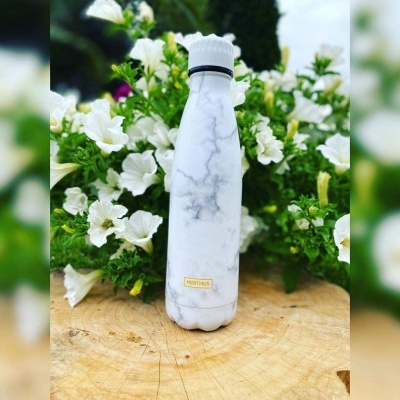 Garrafa térmica branca com padrão marmoreado sobre madeira com flores ao fundo