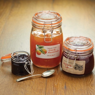 Três frascos de vidro com compotas, tampas metálicas, sobre mesa de madeira