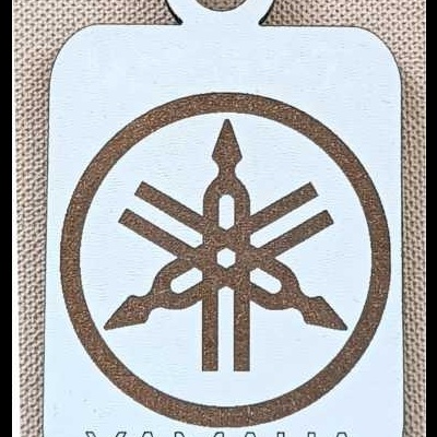 Chaveiro branco com logo Yamaha em ferrugem sobre tecido bege