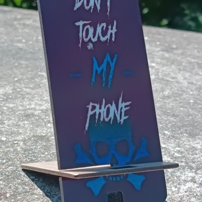 Suporte para telemóvel preto com texto e caveira em superfície de pedra ao ar livre